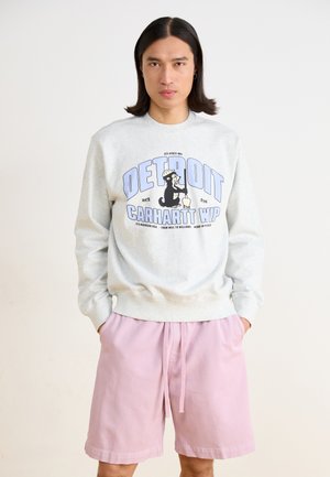 Sweatshirt gris clair avec un texte graphique bleu portant les mots "DETROIT" et "CARHARTT WIP." Associé à un short rose pastel, avec un cordon de serrage élastique.