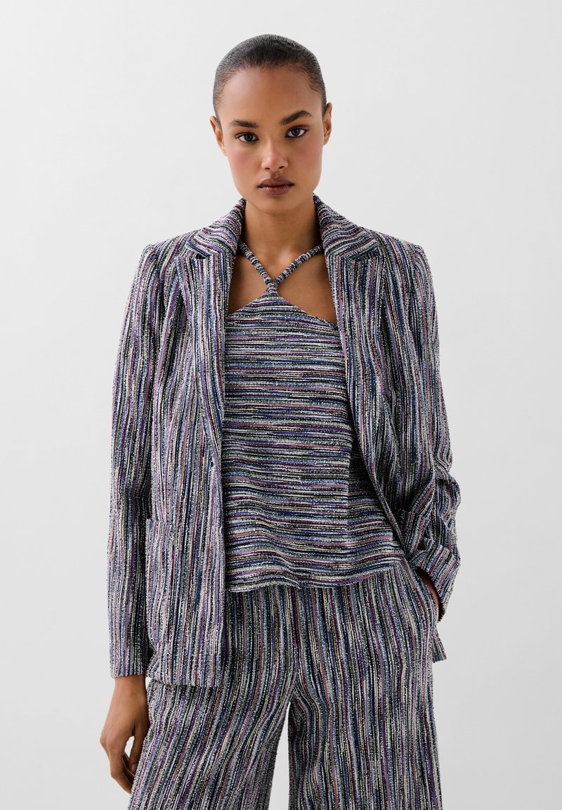Ensemble rayé multicolore composé d'un tissu texturé. Comprend un blazer ajusté, un top sans manches et un pantalon large avec des motifs linéaires.