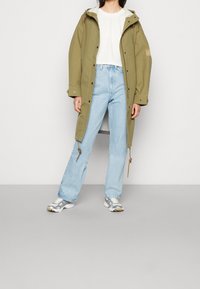 Zielony oliwkowy płaszcz przeciwdeszczowy do kolan z kapturem na sznurek, w połączeniu z jasnoniebieskimi dżinsami i srebrnymi butami sportowymi. Posiada metalowe zatrzaski i boczne kieszenie.