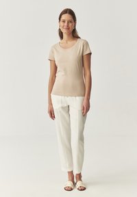 T-shirt beige à manches courtes avec un col rond, associé à un pantalon droit blanc et des sandales à glisser crème clair. Texture lisse.