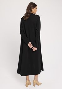 Długi czarny płaszcz o prostym kroju, z ozdobnymi złotymi guzikami na ramionach. Wyposażony w kieszenie boczne i miękką teksturę.