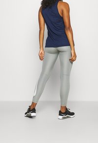 Grå leggings med en vit accentdetalj och en figurnära design, parat med en mörkblå ärmlös topp och svarta löparskor.