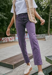 Violetti farkkuhousut suoralla leikillä, yhdistettynä beigeen fleeceliiviin ja valkoiseen t-paitaan. Valkoiset tennarit paksulla pohjalla.