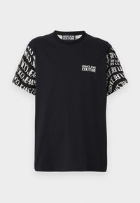 Čierne tričko s krátkym rukávom s bielym nápisom "Versace Jeans Couture" na prednej časti hrudníka a rukávy sú pokryté opakujúcim sa bielym logom.