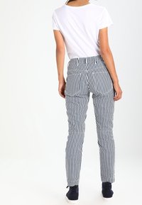 Randiga byxor i marinblått och vitt, med en figurnära design, bakfickor, uppvikta fållar och en midjehöjd som är medelhög. Parat med en enkel vit topp.