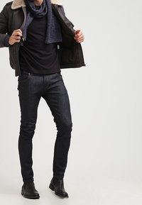 Tummat farkut yhdistettynä mustaan t-paitaan, harmaaseen huiviin ja tumman väriseen bomber-takkiin, jossa on karvakaulus. Mustat nilkkurit viimeistelevät asun.