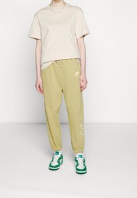 Beige cotton t-shirt with short sleeves, paired with olive green joggers featuring elastic cuffs and Nike branding. Green and white sneakers complete the look.