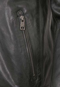Schwarze Lederjacke mit einem Reißverschlussdetail auf der linken Seite. Das Material hat eine glatte Textur, mit kontrastierenden Nähten um den Reißverschluss.