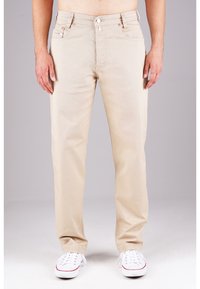 Beige Baumwollhosen mit geradem Bein, fünf Taschen, vornem Knopfverschluss und dezenten Steppdetails. Kombiniert mit weißen Sneakers.