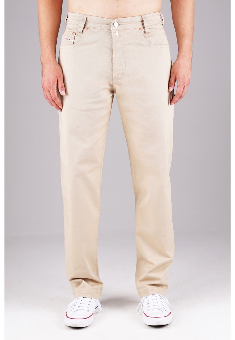 Beige Baumwollhosen mit geradem Bein, fünf Taschen, vornem Knopfverschluss und dezenten Steppdetails. Kombiniert mit weißen Sneakers.
