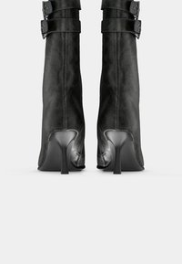 Black leather ankle boots with a tapered silhouette, featuring two adjustable straps and buckle details. Stiletto heels complete the design.