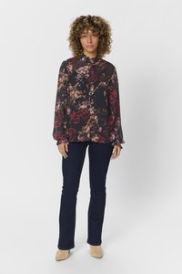 Blusa nera fluida con motivo floreale colorato; presenta un colletto alto e maniche lunghe; abbinata a jeans blu scuro e mule beige.