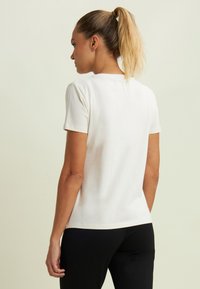 T-shirt bianco in cotone con maniche corte, collo tondo e silhouette aderente, abbinato a pantaloni neri, visto da dietro.