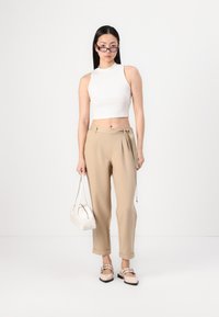Hvit, cropped ermeløs topp, beige høyt liv bukser med belte, hvit veske, og beige leiligheter med dekorativ spenne. Minimalistisk design.