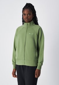Felpa verde con zip, maniche raglan, tasche laterali e un piccolo logo sul petto. Texture morbida e vestibilità comoda.