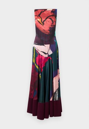 Kobieta w sukience bez rękawów sięgającej podłogi z kolorowym abstrakcyjnym motywem kwiatowym i ciemnofioletowym wykończeniem, stojąca z jedną ręką na biodrze.