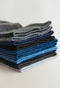 Stapel aus gestrickten Tüchern in verschiedenen Blautönen, Grau und Schwarz. Strukturierter Stoff mit sauberen Kanten, der ein durchdachtes Design präsentiert.