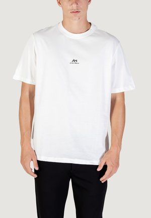 Witte katoenen t-shirt met korte mouwen, met een klein zwart logo op de borst. Het ontwerp is eenvoudig met een ronde hals.