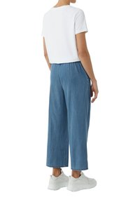 Witte kortemouwenshirt, losse lichtblauwe jeans en grijze sneakers. De jeans hebben een elastische tailleband en zijzakken.