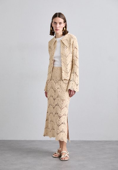 Beige crocheted two-piece set featuring a blouse with a buttoned front and a knee-length skirt with a slit, displaying an intricate pattern.