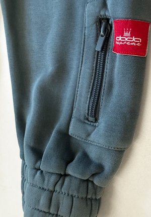 Dunkelblaue Jogginghose aus weichem Stoff mit einer Reißverschlusstasche und einem roten Logopatch mit Kronendesign an der Seite.