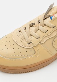 Beige lädersneakers med perforerad ovandel, platta snören och gummisula. Har sömnadsdetaljer och en kontrasterande logotyp på tungan.