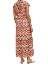 Robe maxi avec un motif en zigzag dans des tons orange, rose et marron, avec des manches courtes et une taille élastique. Portée avec des sandales blanches.