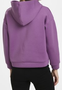Sweat à capuche violet en tissu doux, avec une grande capuche, des épaules tombantes et une coupe décontractée avec un ourlet côtelé et des poignets.