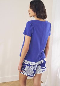 Blue cotton t-shirt with short sleeves and a relaxed fit, paired with white shorts featuring a large floral pattern.