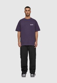 Lilla bomulds T-shirt med korte ærmer og brystlogo, parret med sorte cargo bukser. Outallen har en afslappet pasform og et casual design.