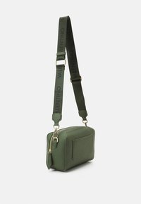Zelená obdélníková kožená crossbody taška s širokým nastavitelným popruhem, na kterém je černý text "Valentino", zlatý zip a kovové detaily.