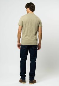 Menns olivengrønn t-skjorte med korte ermer, kombinert med mørkeblå jeans. Stoffet ser mykt og tettsittende ut. Brune sko synlige nedenfor.