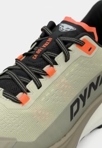 Ανοιχτό γκρι αθλητικό παπούτσι με μαύρες και πορτοκαλί λεπτομέρειες, υφή στη επιφάνεια, πλέγμα και ανακλαστικά λογότυπα, διαθέτοντας μια ανθεκτική σόλα.