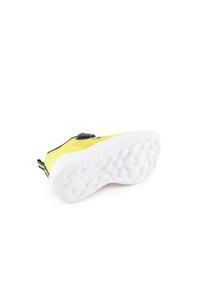 Zapatilla amarilla con parte superior texturizada, acentos negros y suela de goma blanca con patrones circulares para mayor agarre. Correa de Velcro para un ajuste seguro.
