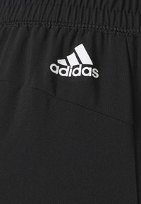 Shorts de sport noirs en tissu léger, avec une taille élastique et un logo Adidas blanc sur le devant.