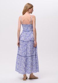 Robe maxi en bleu clair avec imprimé floral, corsage smocké, bretelles fines et jupe à volants. Tissu lisse et coupe décontractée.