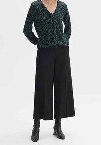 Pantaloni neri a gamba larga abbinati a una maglietta a maniche lunghe verde scuro a fantasia con scollo a V. Tessuto testurizzato, vestibilità slim.