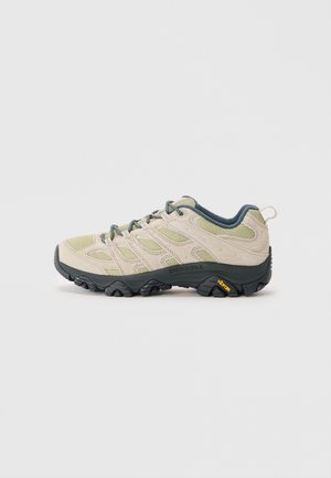 Light beige hiking shoe with green accents, mesh and suede materials, textured sole with pronounced tread, and Vibram branding on the heel.