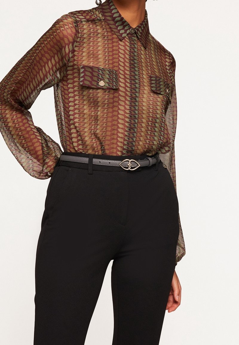 Blusa trasparente e a fantasia in toni terreni di bordeaux e verde, con apertura frontale a bottoni, colletto e due tasche sul petto. Abbinata a pantaloni neri.
