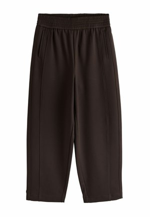 Kéz pihen barna, rugalmas derékpántos nadrág mellett, amelyen függőleges hasított zseb található, két aranygyűrűvel, vörös és fekete kövekkel viselve.