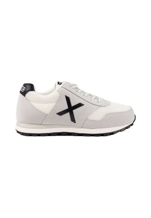Zapatilla deportiva blanca y gris con logo "X" negro en el lateral, paneles de malla, cierre de cordones y suela negra.