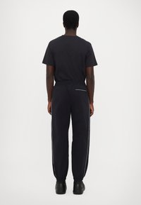 Zwarte katoenen t-shirt en bijpassende broek met elastische taille, taps toelopende benen, zijstrepen en achterzak. Duurzaam materiaal, minimalistisch ontwerp.