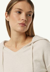 Helle beige Kapuzenpullover mit V-Ausschnitt und Kordeln. Weicher Stoff, figurbetontes Design und sichtbare Nähdetails am Kragen.