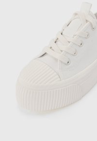 Baskets blanches en toile avec un bout arrondi, semelle en caoutchouc nervurée et lacets plats. Elles présentent une couture latérale et un embout texturé.
