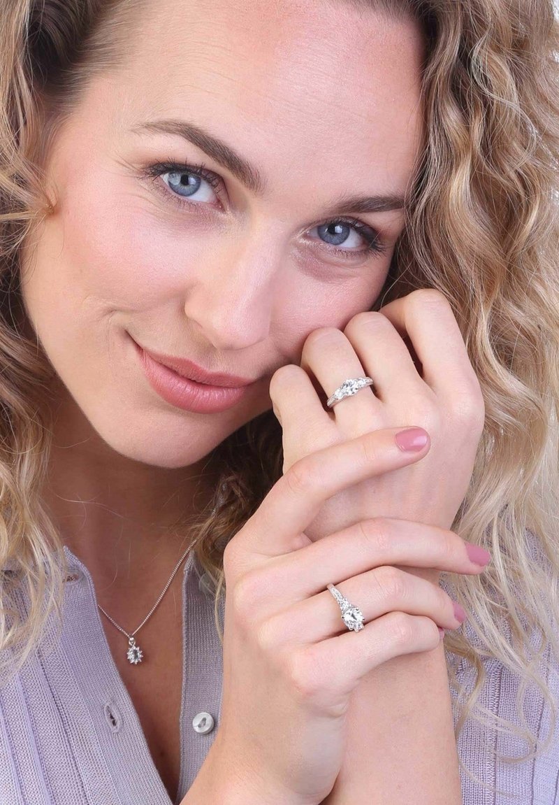 Silver jewelry featuring a decorative pendant necklace and intricately styled rings with clear stones, set against a light background.
