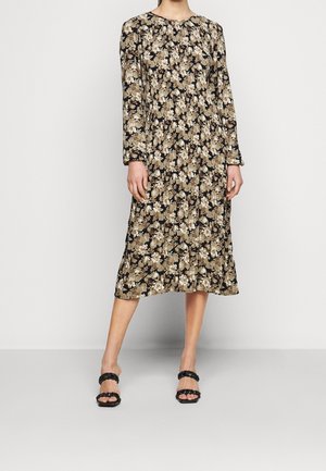 Langärmliges Blumenkleid in Schwarz mit cremefarbenen und beigen Mustern. Es hat einen runden Ausschnitt und eine fließende Silhouette. Kombiniert mit schwarzen Sandalen.
