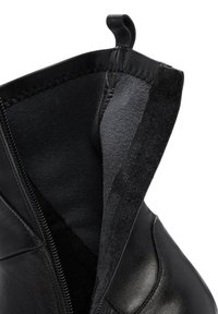 Gros plan sur une botte en cuir noir avec une fermeture éclair partiellement ouverte, montrant l'extérieur en cuir lisse et la doublure intérieure douce et sombre.