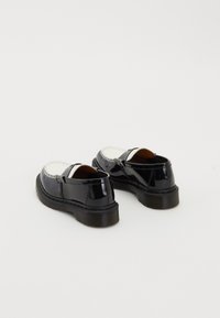 Zwart-witte leren loafers met dikke zwarte zolen, gezien van achteren op een witte achtergrond.