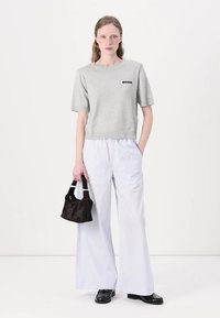 Cropped top grigio a maniche corte con logo nero, abbinato a pantaloni larghi a righe bianche e una piccola borsa nera. Presenti mocassini neri.
