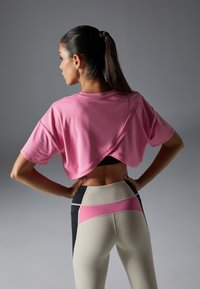 Rosa verkürztes T-Shirt mit einem verdrehten Rücken-Design, kombiniert mit hochgeschnittenen Leggings, die Beige-, Rosa- und Schwarzfarbblockierungen aufweisen.